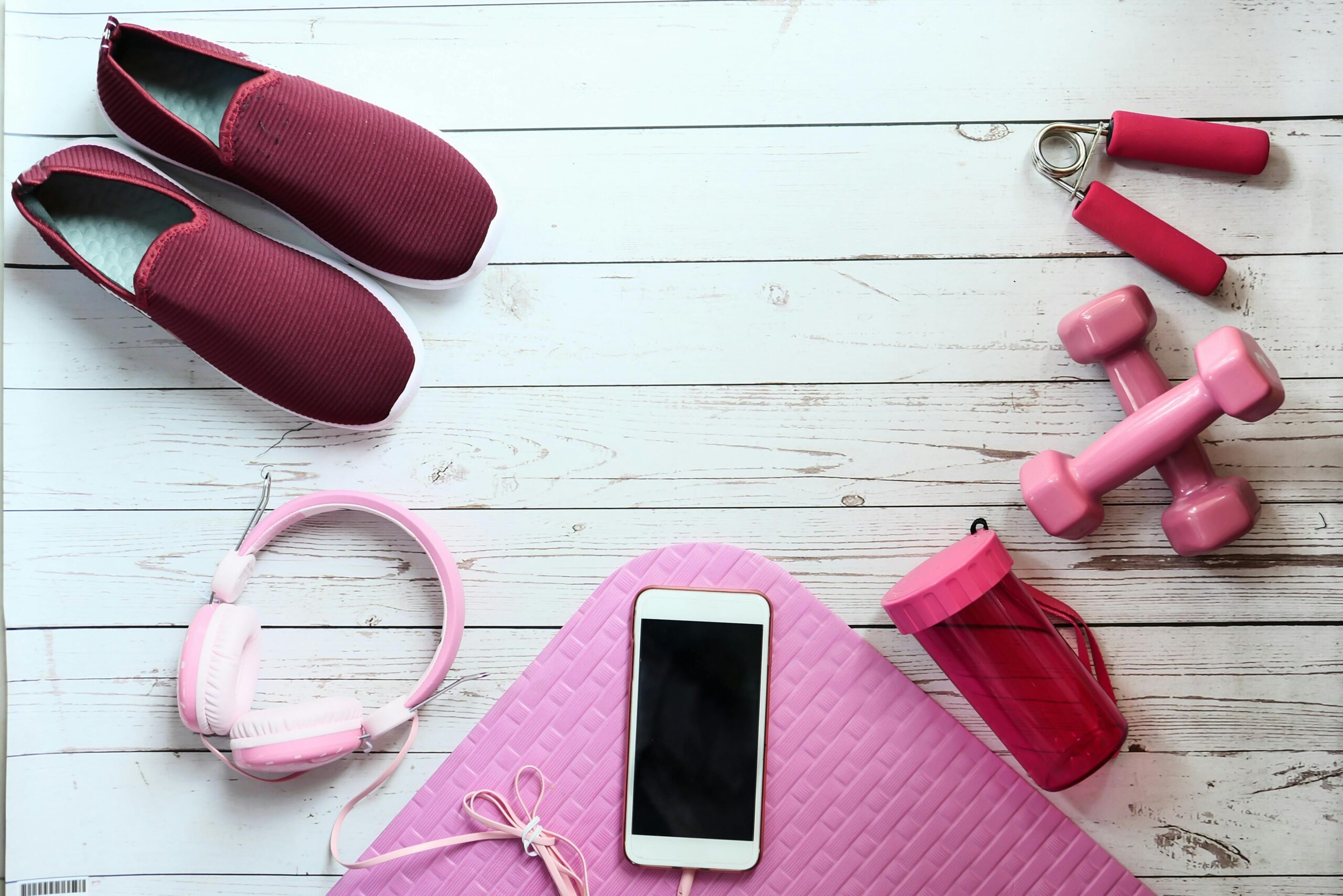 A flat lay of pink fitness items on white wood, ideal for lifestyle imagery.
